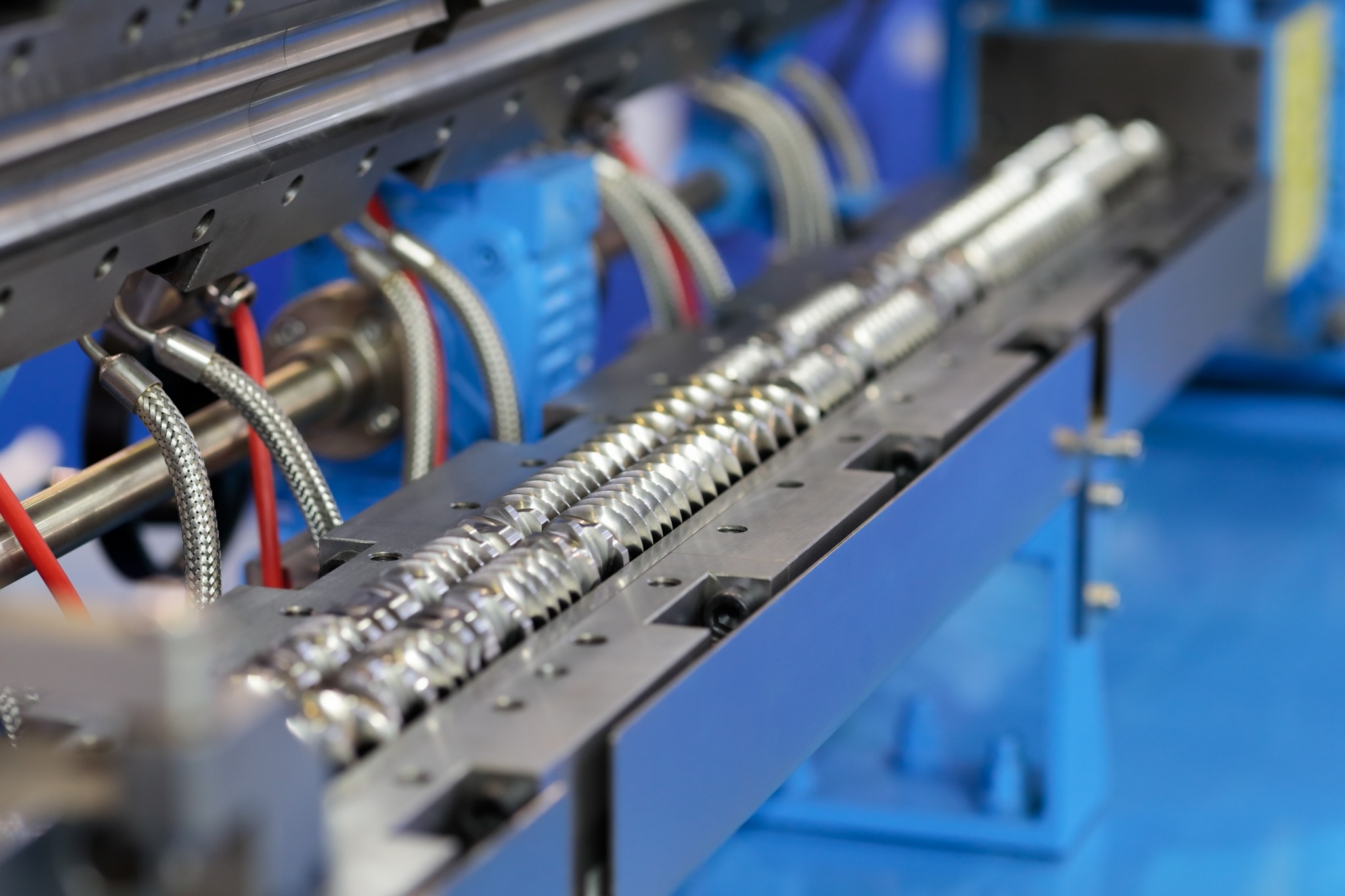 Close-up of intermeshing twin screws in blue polymer extrusion equipment